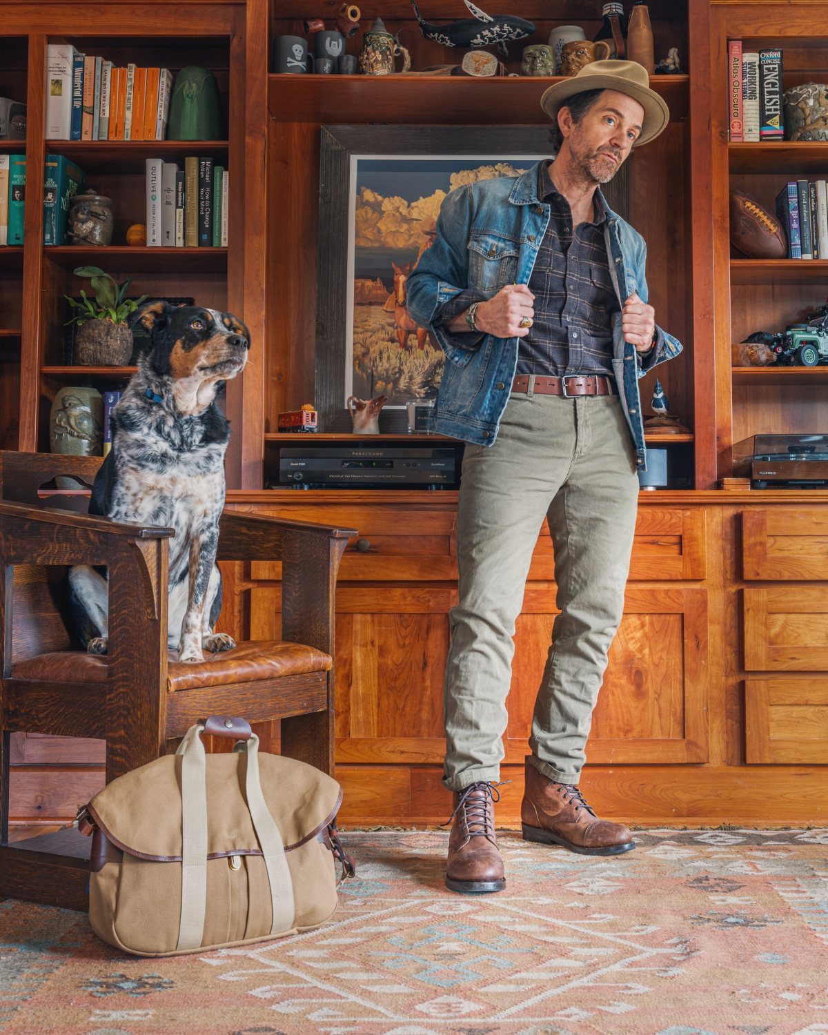 Man in denim jacket and khaki pants wearing brown leather boots in library