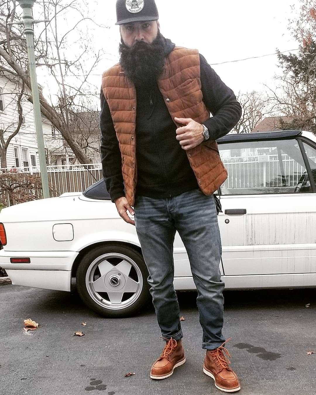 Man with beard wearing brown boots, blue jeans, and brown quilted vest.
