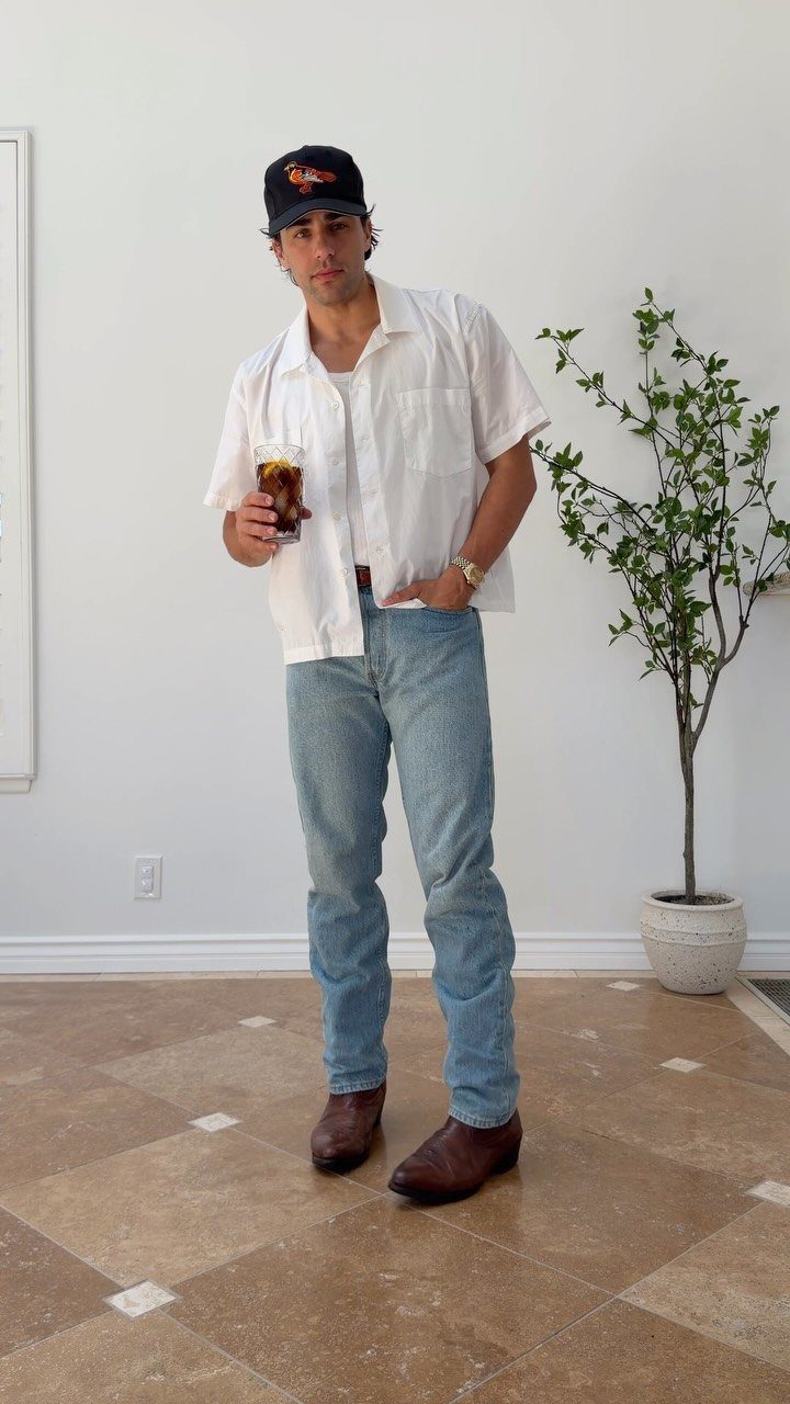 Man in white shirt and light blue jeans wearing brown leather boots.