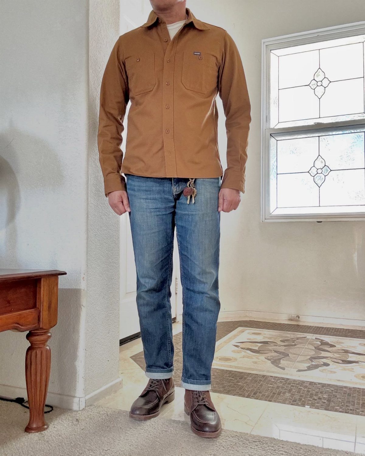 Man wearing brown shirt, blue jeans, and dark brown leather brogue shoes.