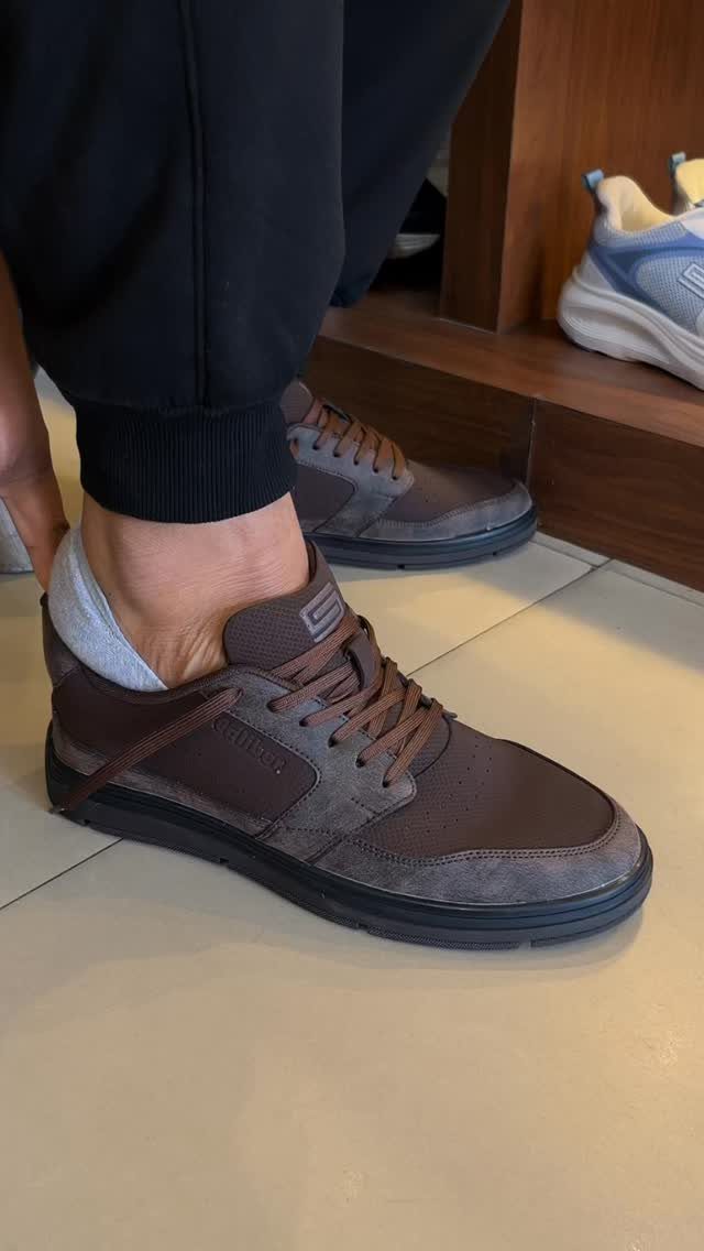 Brown casual sneakers with black joggers and grey socks on a tiled floor.