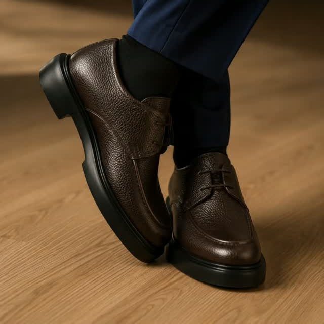 Dark brown pebbled leather derby shoes paired with dark blue trousers on wooden floor
