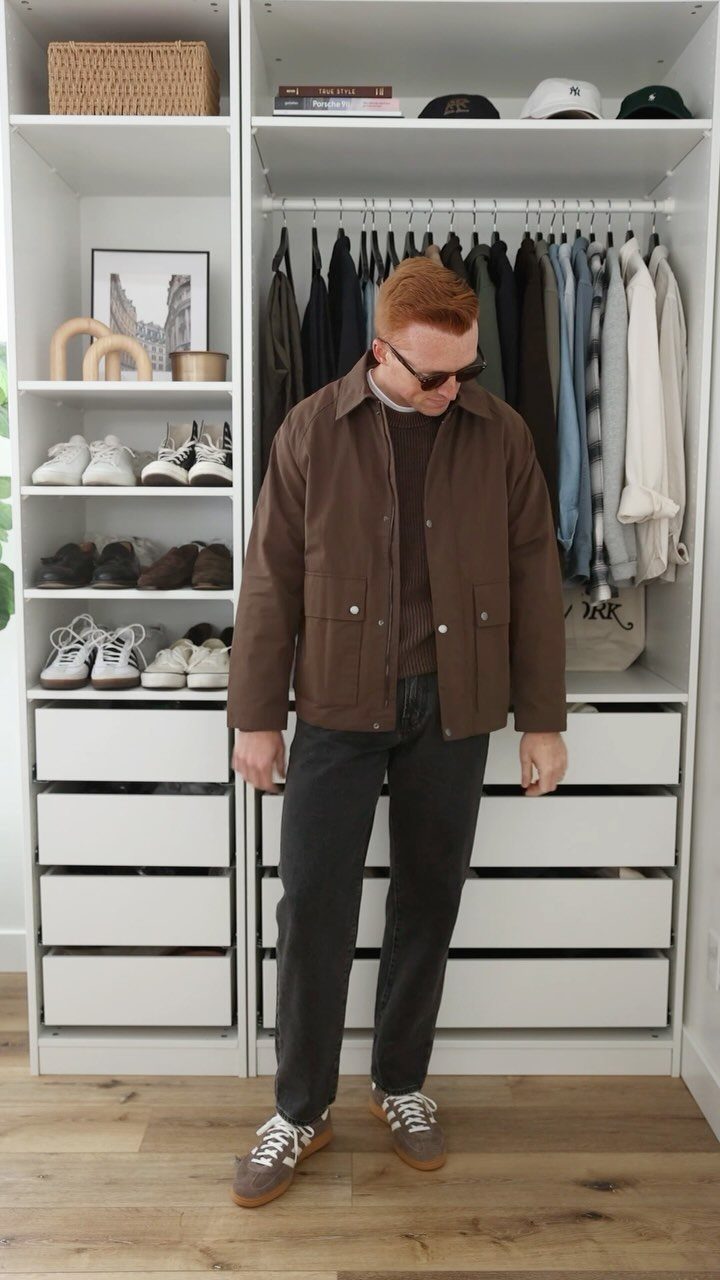 Man wearing a brown jacket and brown sneakers standing in a white closet.