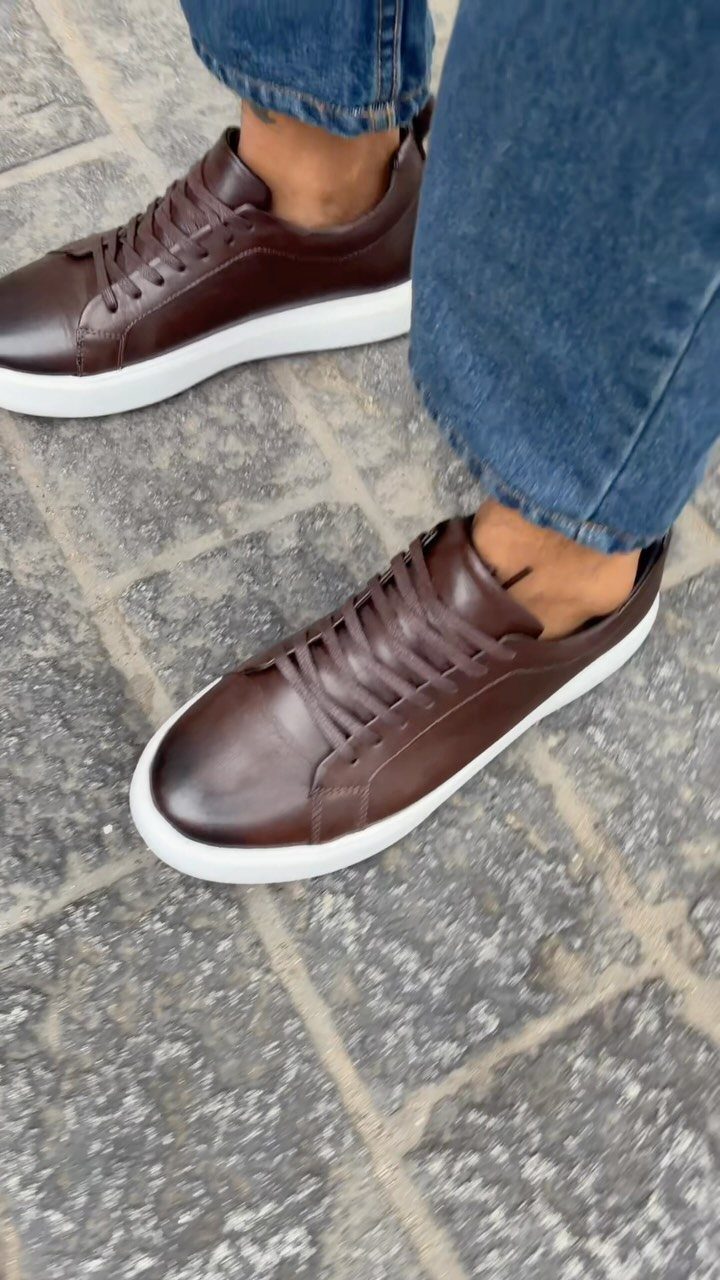 Brown leather sneakers with white soles paired with blue denim jeans on pavement