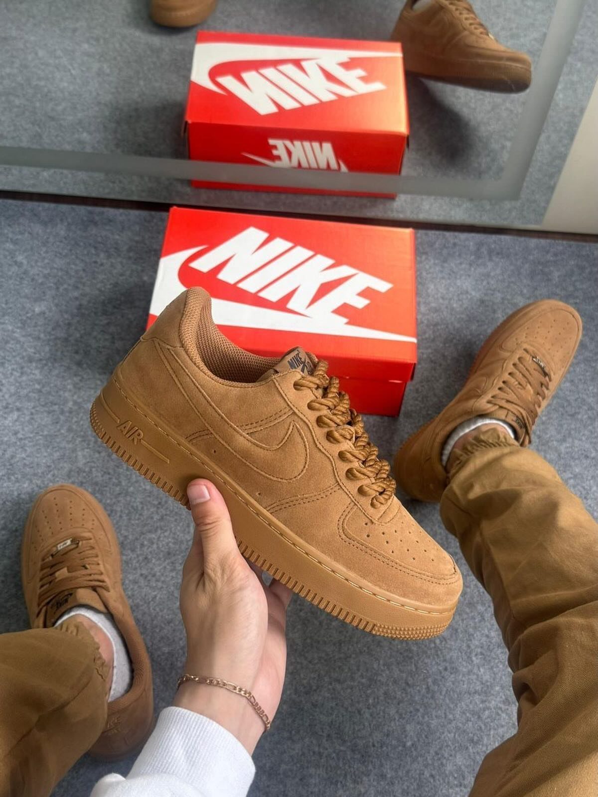 Brown suede Nike sneakers paired with matching brown trousers on a grey carpet.