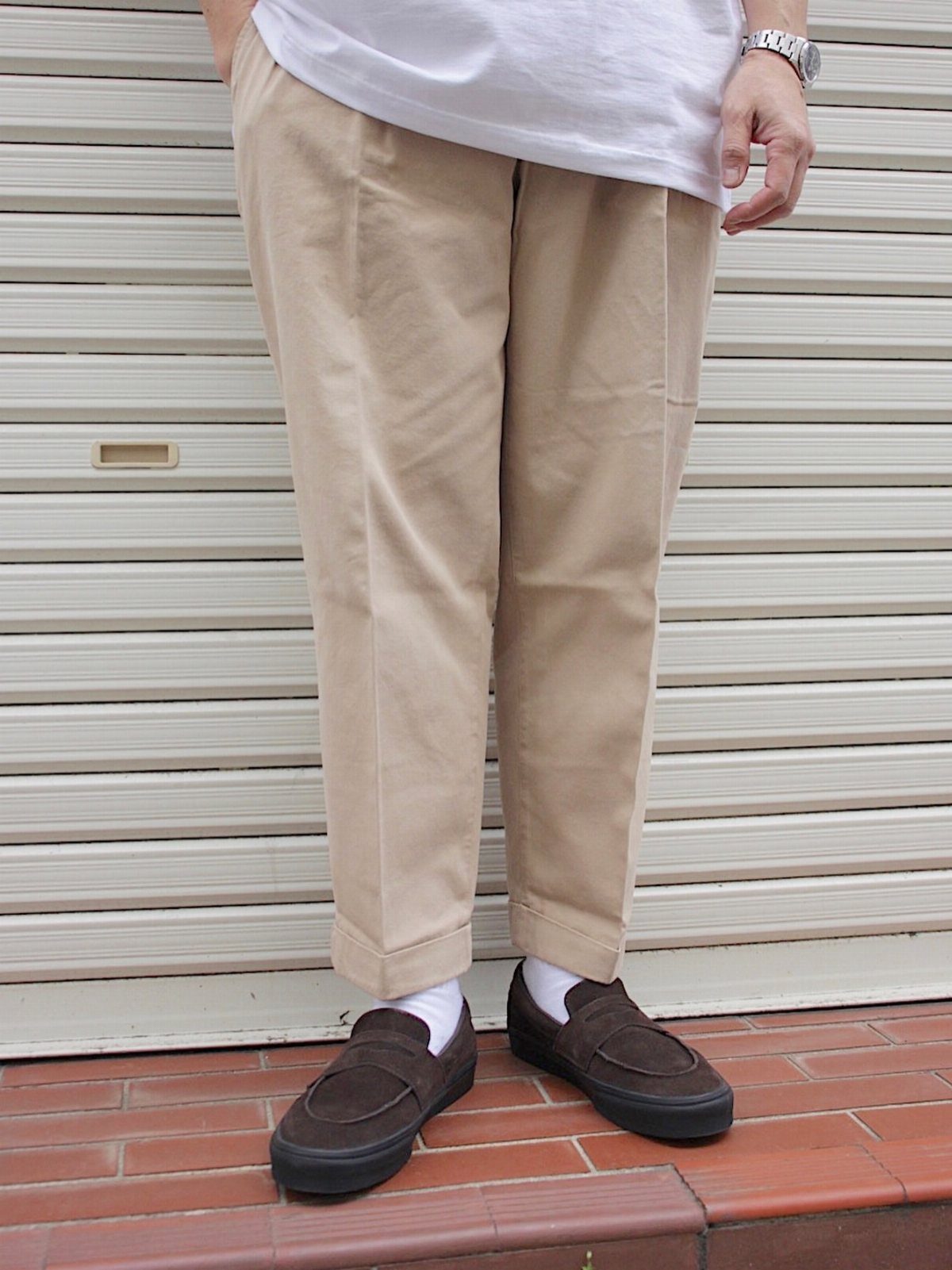 Dark brown suede loafers worn with beige cropped pants and white socks.