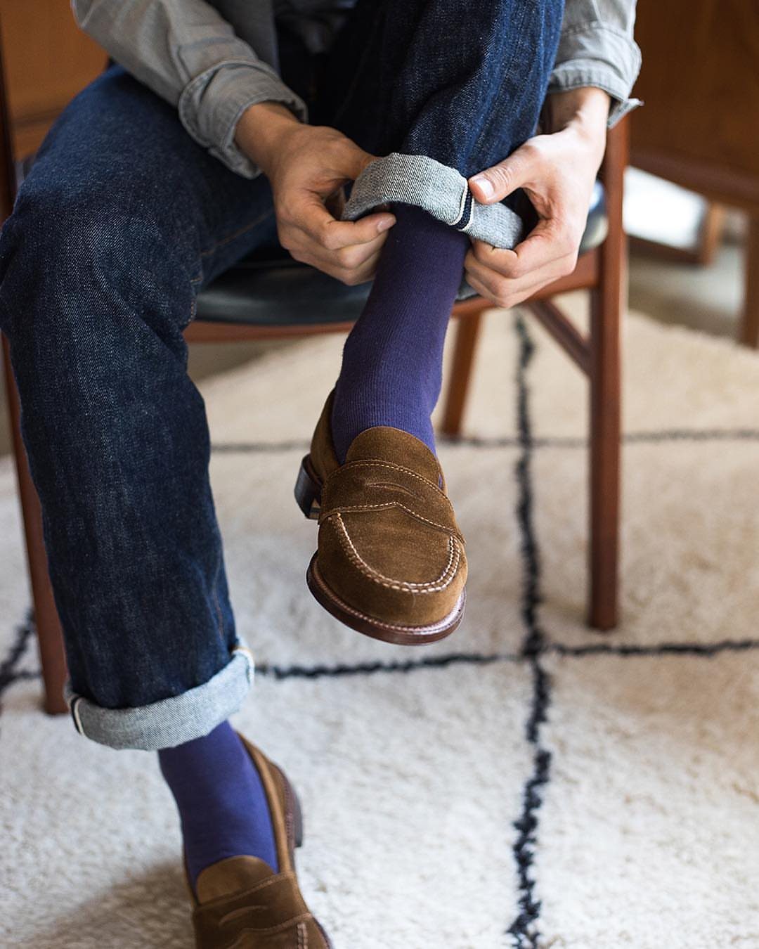 Brown suede loafers paired with dark blue denim jeans and purple socks.
