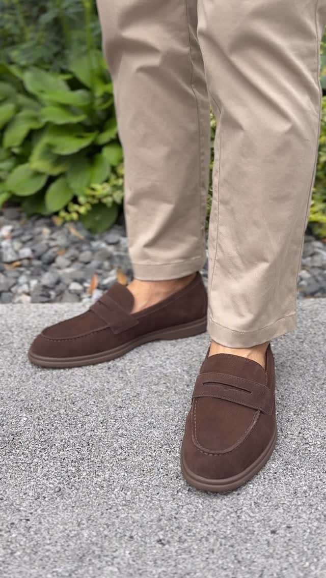 Dark brown suede loafers paired with beige chino pants on a concrete path.