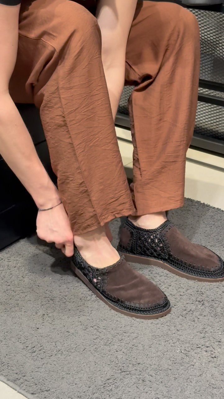 Brown suede loafers with woven sides worn with brown textured trousers on grey rug