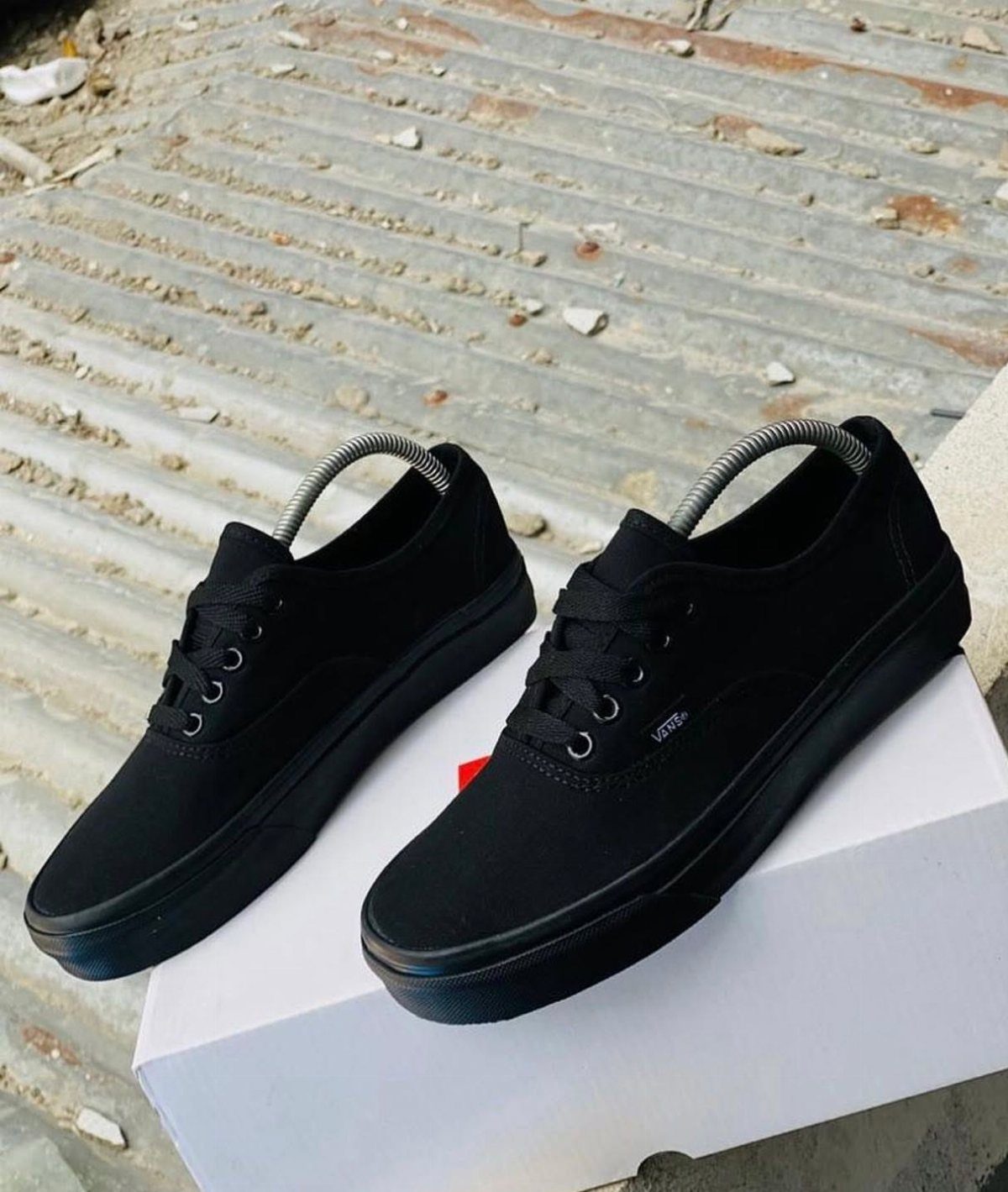 Black canvas sneakers with black laces resting on a white shoebox.