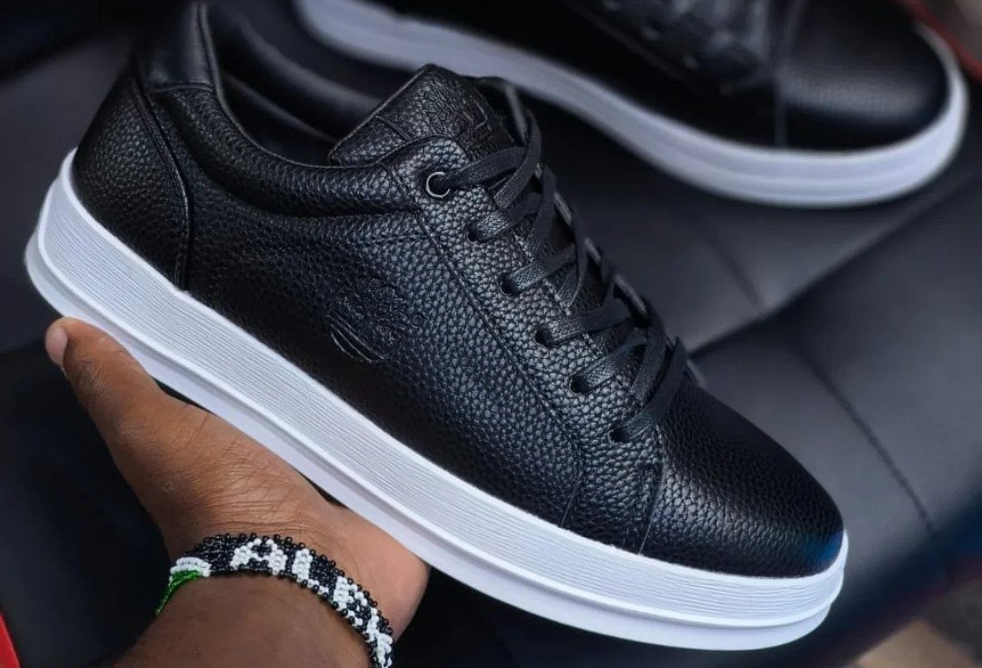 Black pebbled leather sneakers with white soles held by a person's hand.
