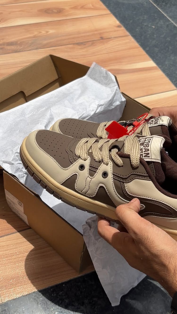Brown and beige chunky sneakers held over a cardboard shoebox on wooden decking.