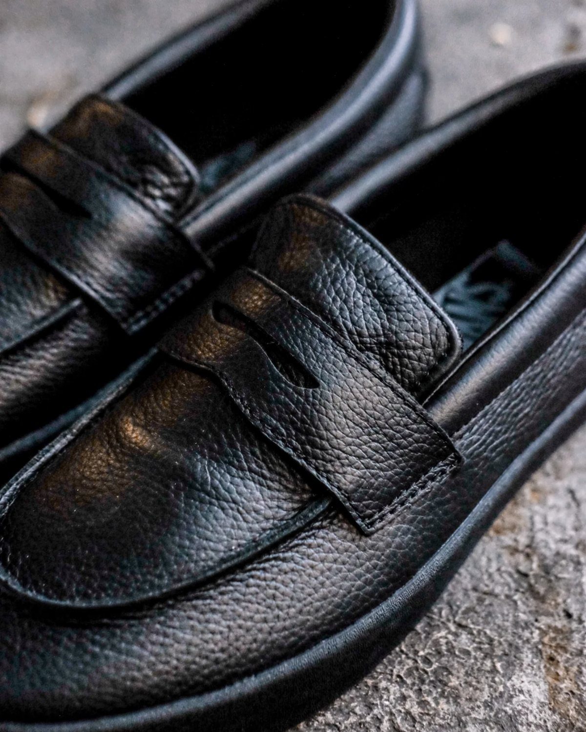 Black leather loafers with pebbled texture resting on a grey stone surface.