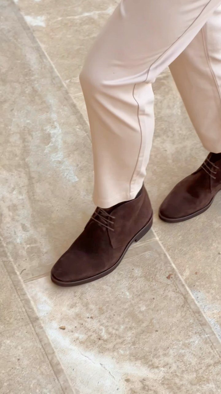 Dark brown suede chukka boots paired with light beige chino trousers on stone flooring.