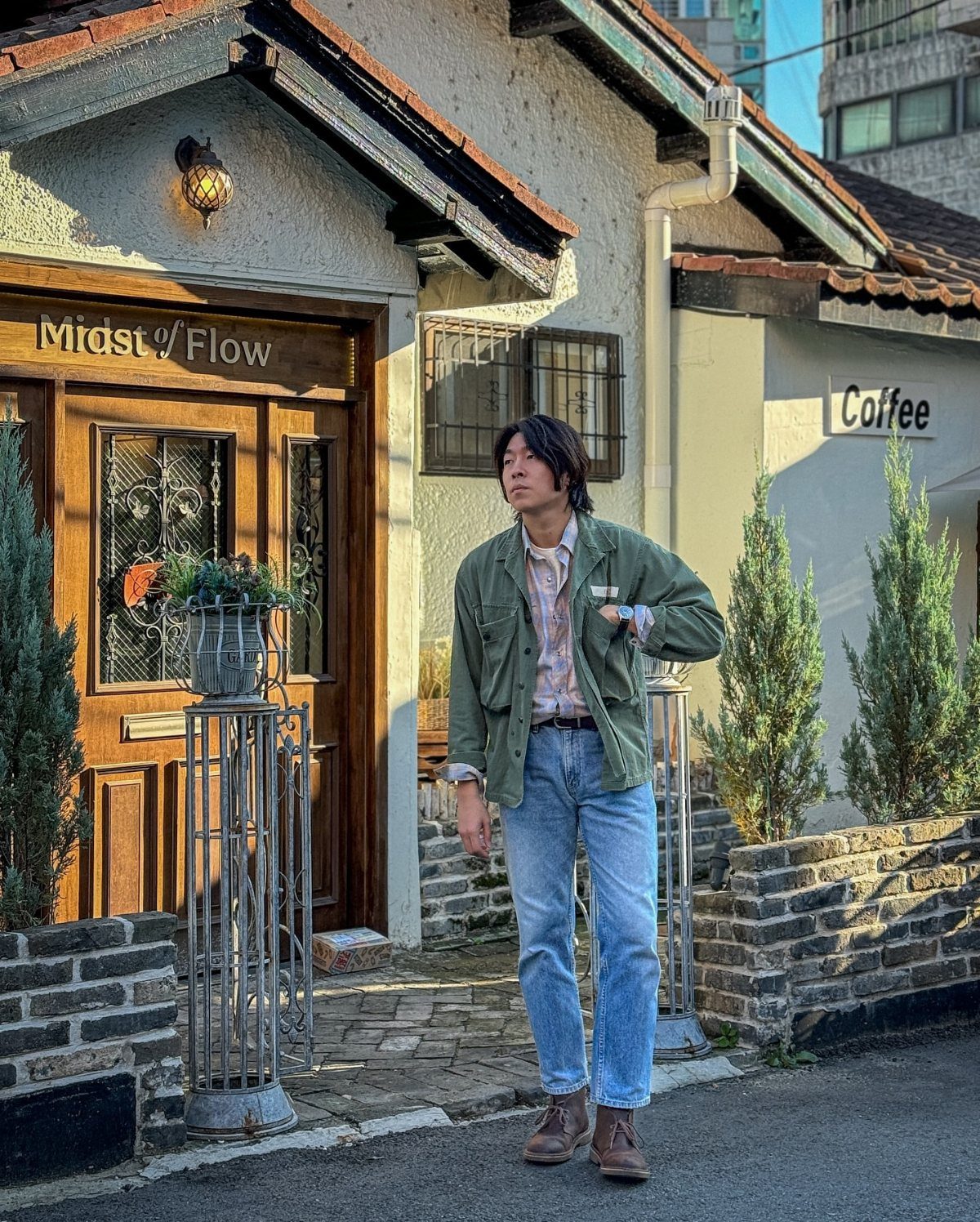 Man wearing a green jacket, light blue jeans, and brown suede chukka boots.