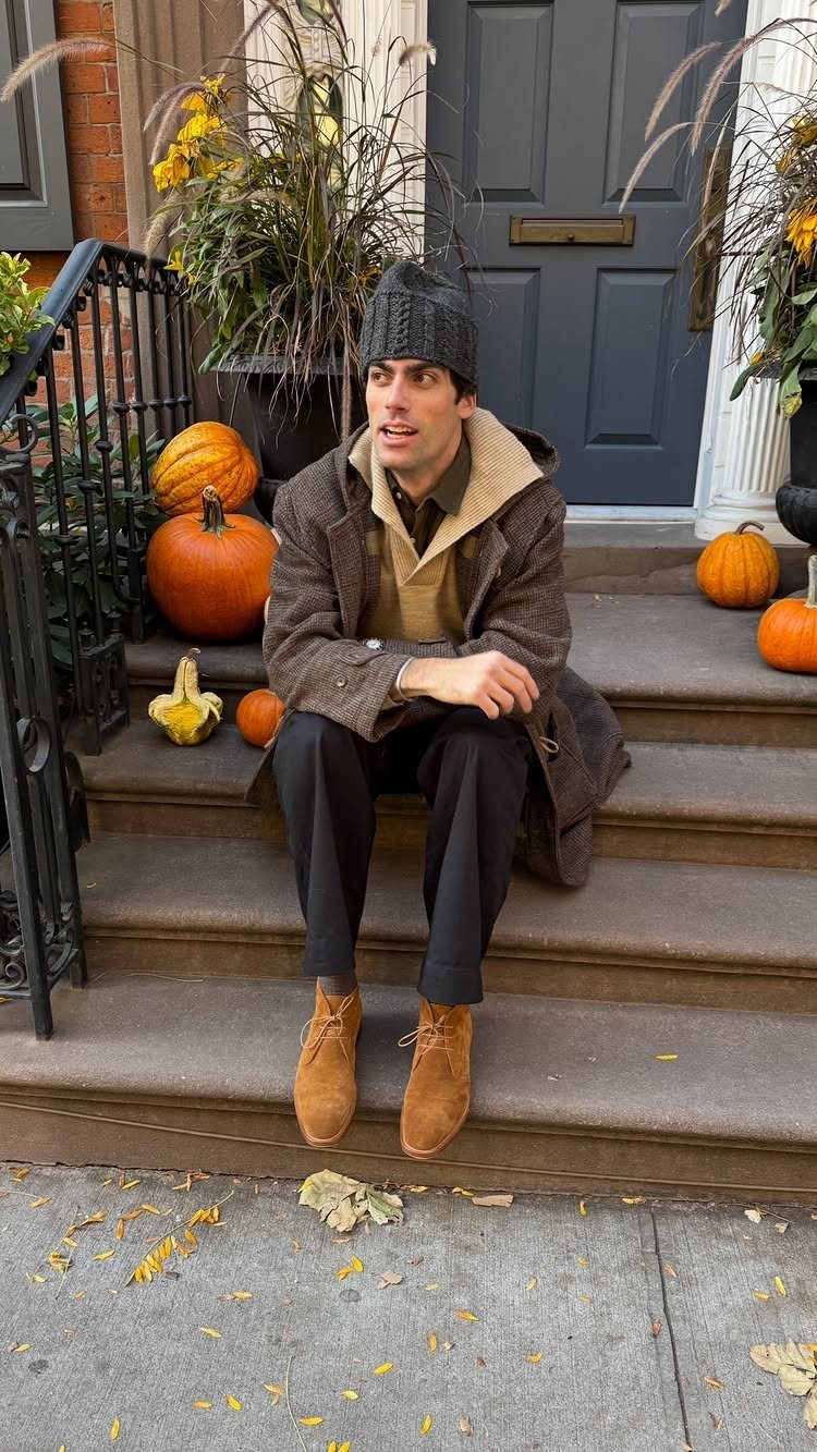 Man in a grey overcoat and tan chukka boots sitting on autumn steps.