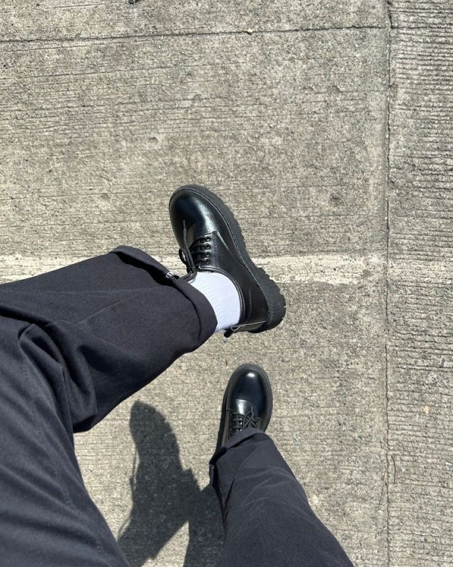 Black chunky derby shoes and black trousers on a grey concrete surface.