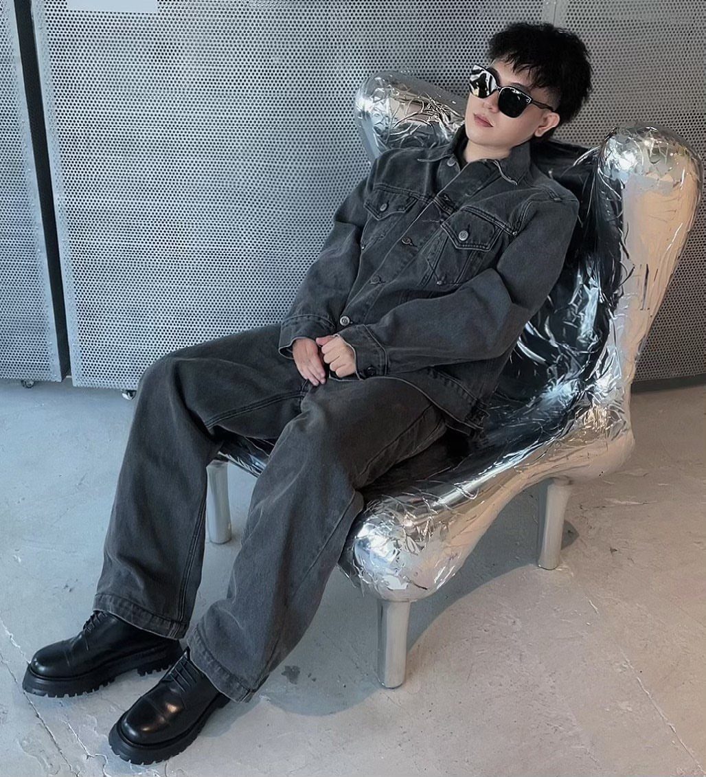 Person in grey denim outfit and chunky black derby shoes sitting in silver chair