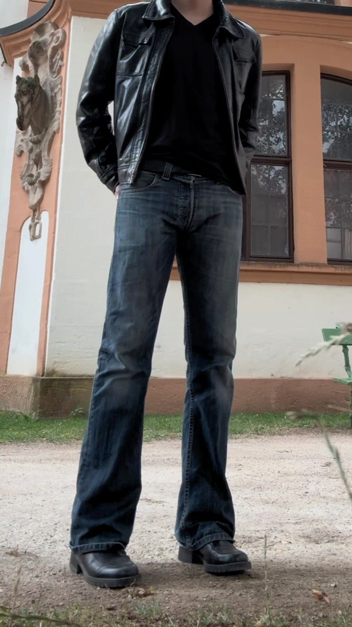 Person wearing black chunky derby shoes, flared blue jeans, and a leather jacket.