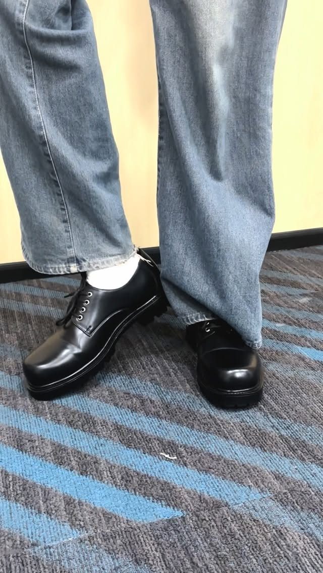 Black leather chunky derby shoes paired with light blue jeans and white socks.