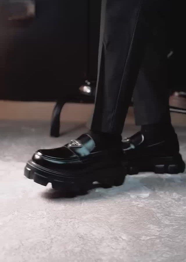 Black chunky derby shoes with thick soles paired with black trousers on concrete.