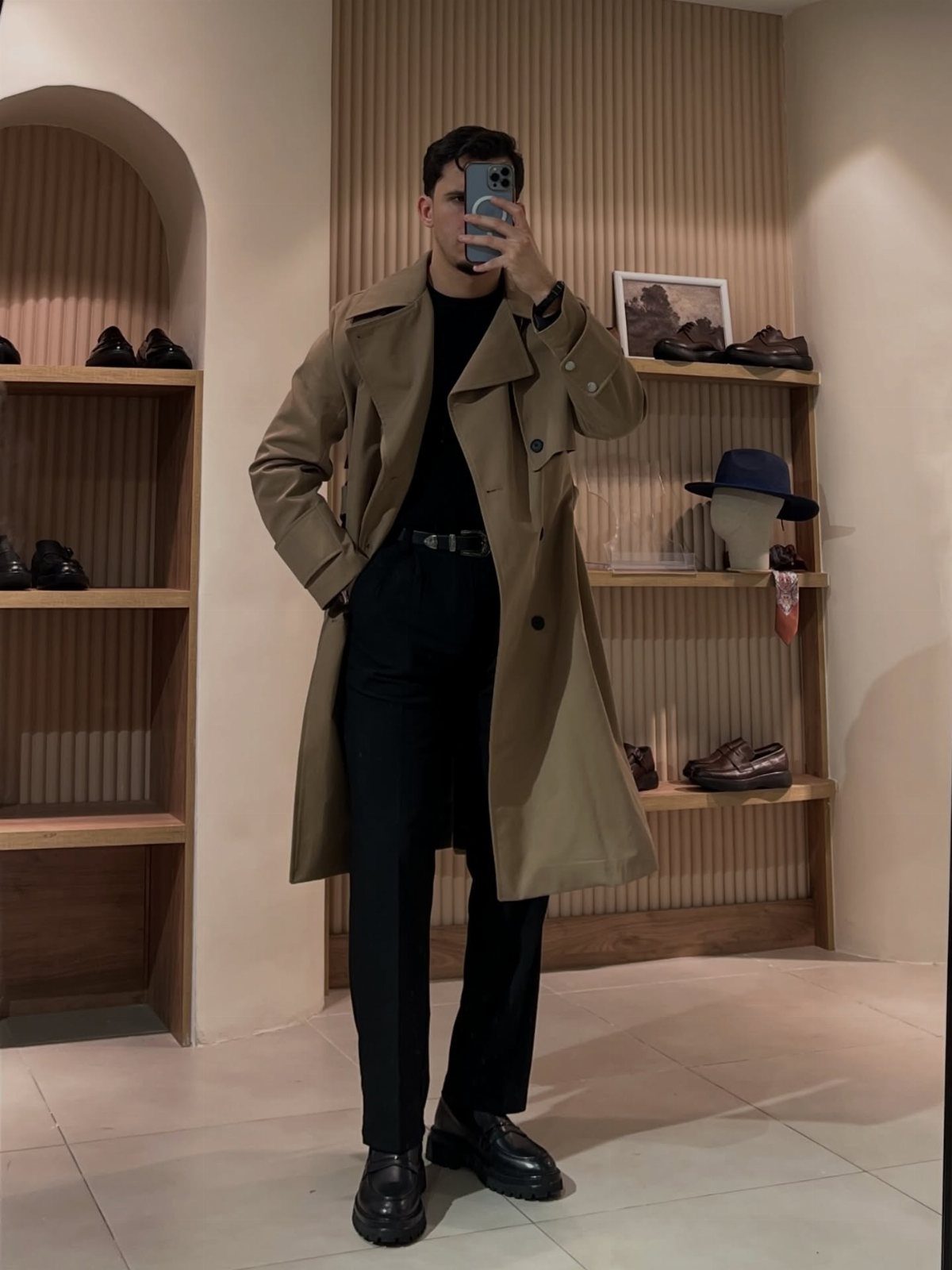 Man wearing a tan trenchcoat, black trousers, and black chunky derby shoes.