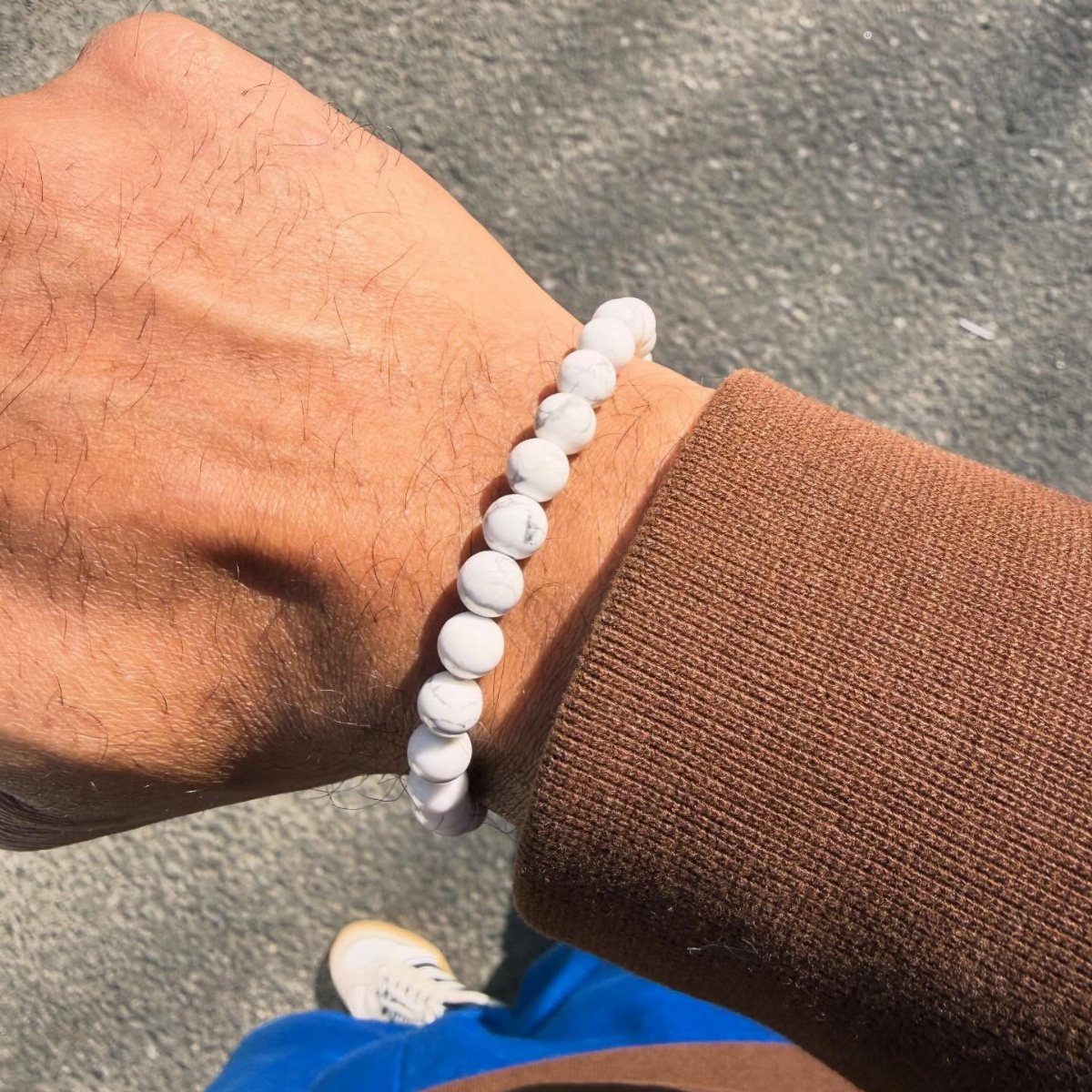 White howlite bead bracelet worn on a man's wrist with a brown sweater.