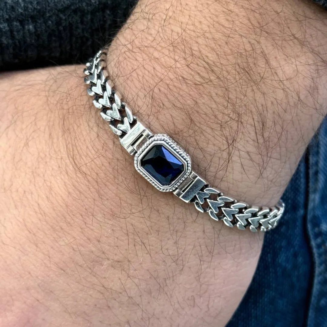 Silver curb chain bracelet with a dark blue crystal on a man's wrist