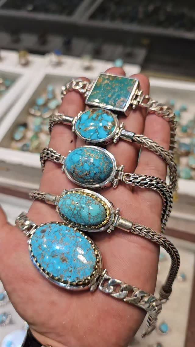 Five silver bracelets with turquoise stones held in a person's open palm.