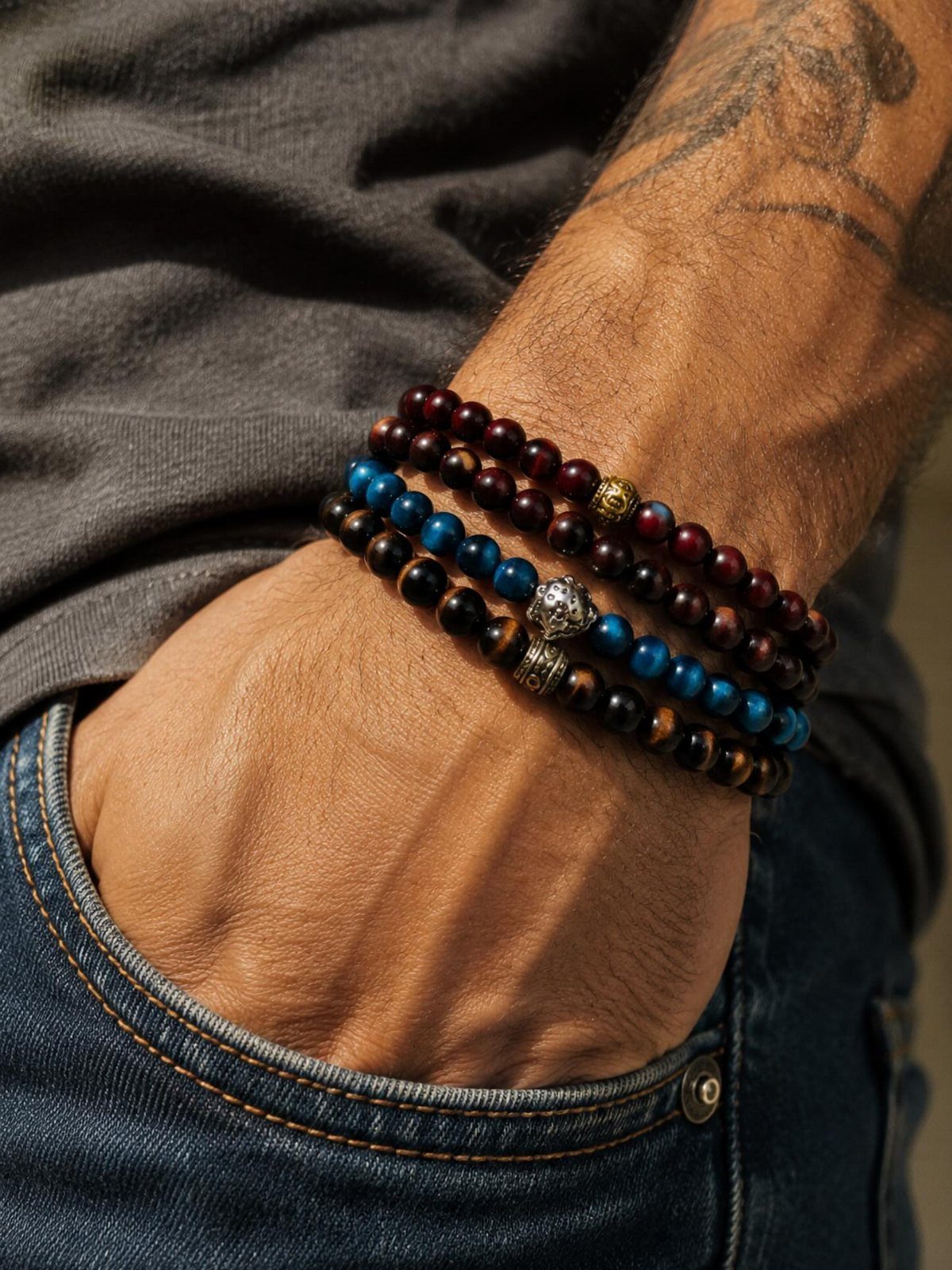 Three beaded crystal bracelets on a man's wrist with blue jeans and grey shirt