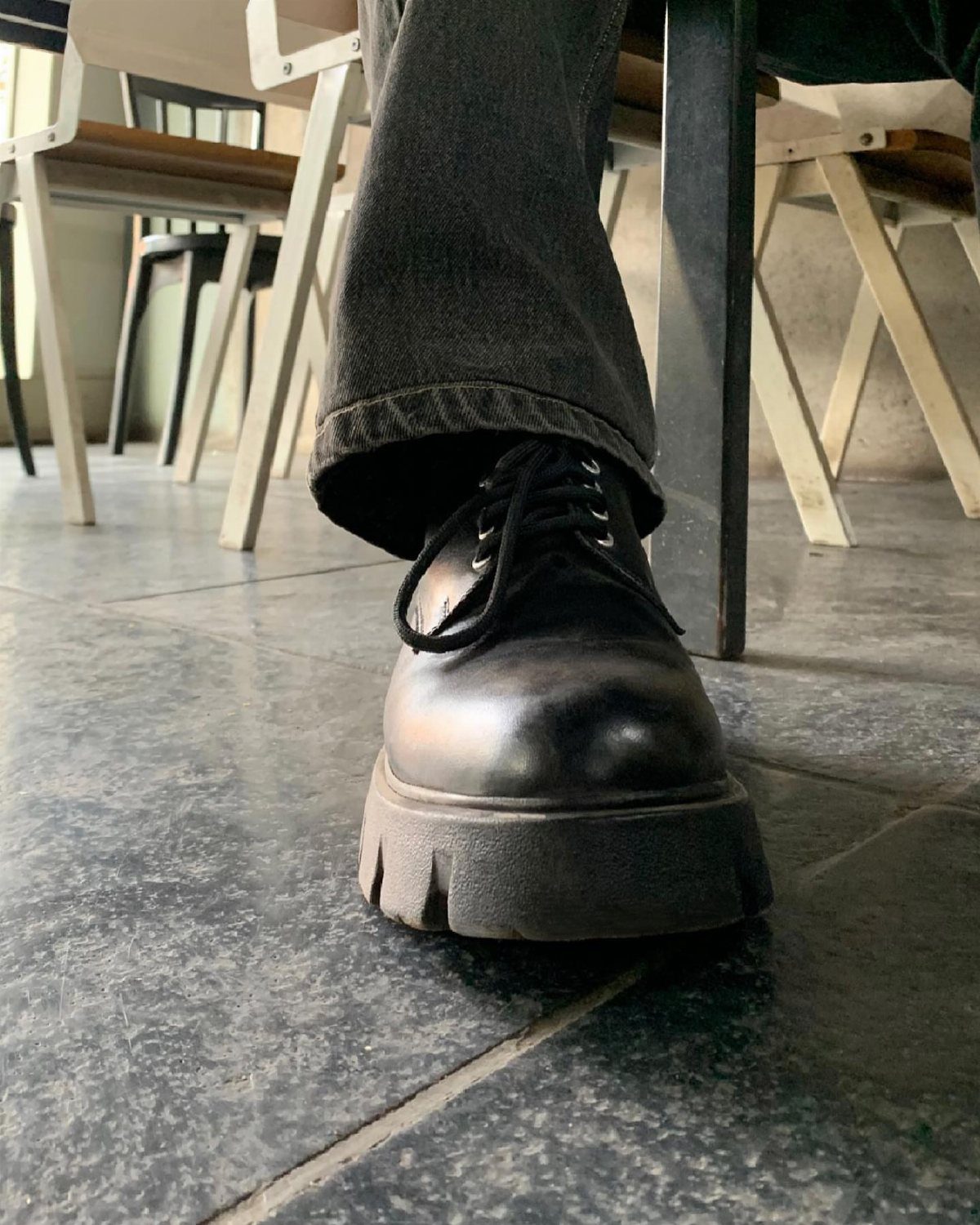 Chunky black leather derby shoes paired with dark grey denim jeans on tiled floor