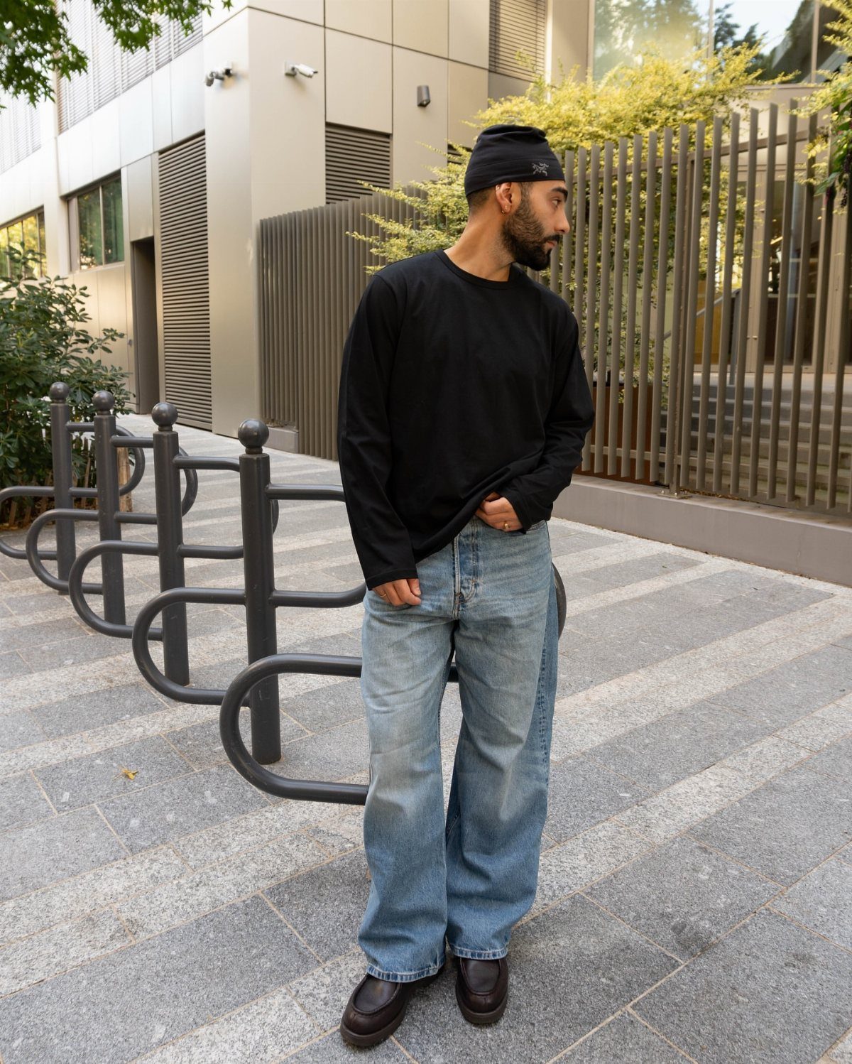 Man wearing wide-leg light blue jeans and dark brown leather derby shoes outdoors.