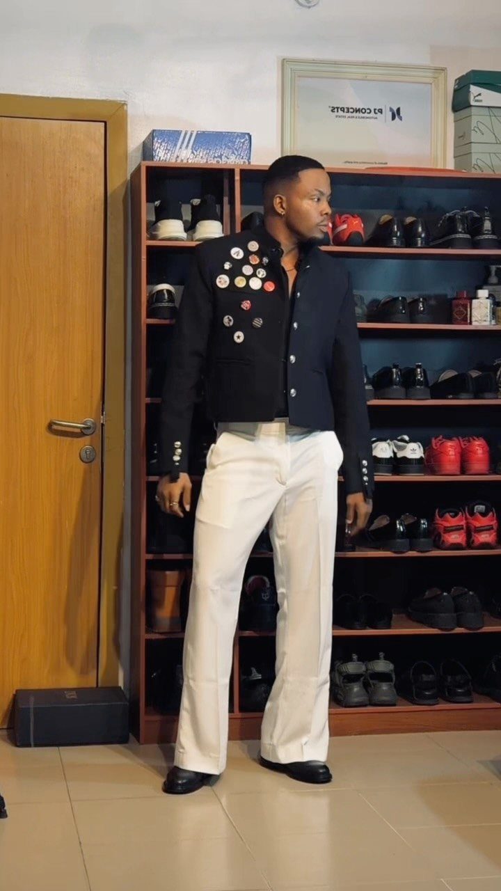 Man in black military jacket and white trousers wearing black leather derby shoes.