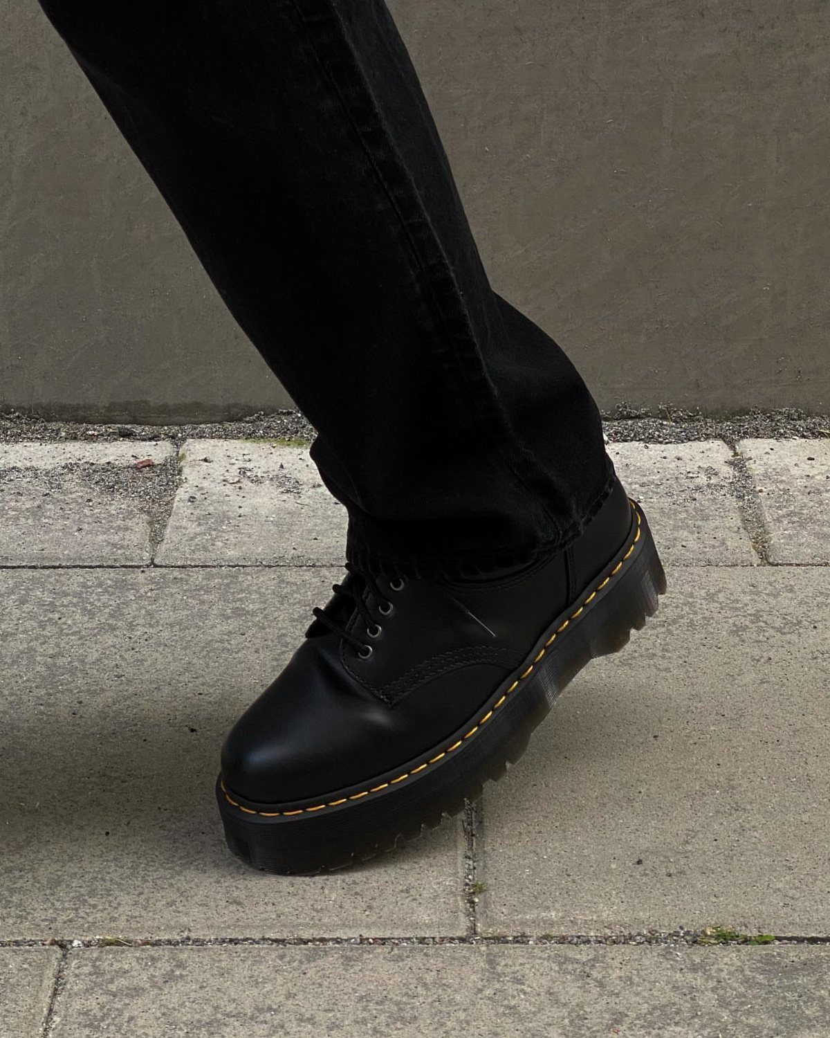 Black leather combat boots and black skinny jeans on a stone pavement.