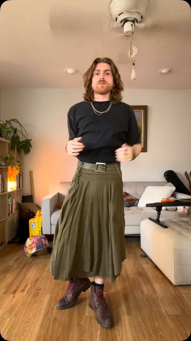 Person wearing a black t-shirt and olive green pleated midi skirt with boots.