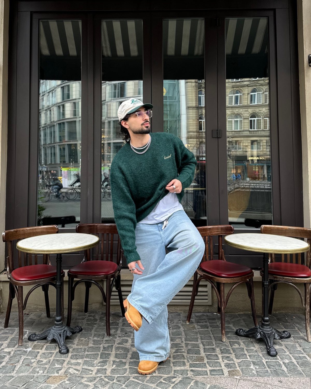 Man wearing a dark green oversized knit sweater and light blue wide-leg jeans.