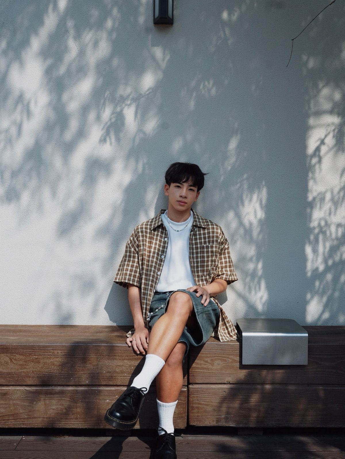 Person wearing a brown plaid shirt, white t-shirt, denim shorts, and black boots.
