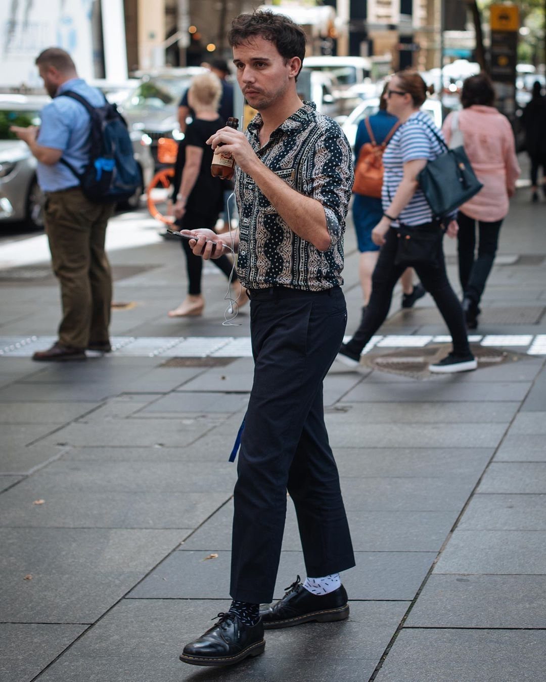 Man in patterned shirt and navy trousers wearing black leather combat boots.