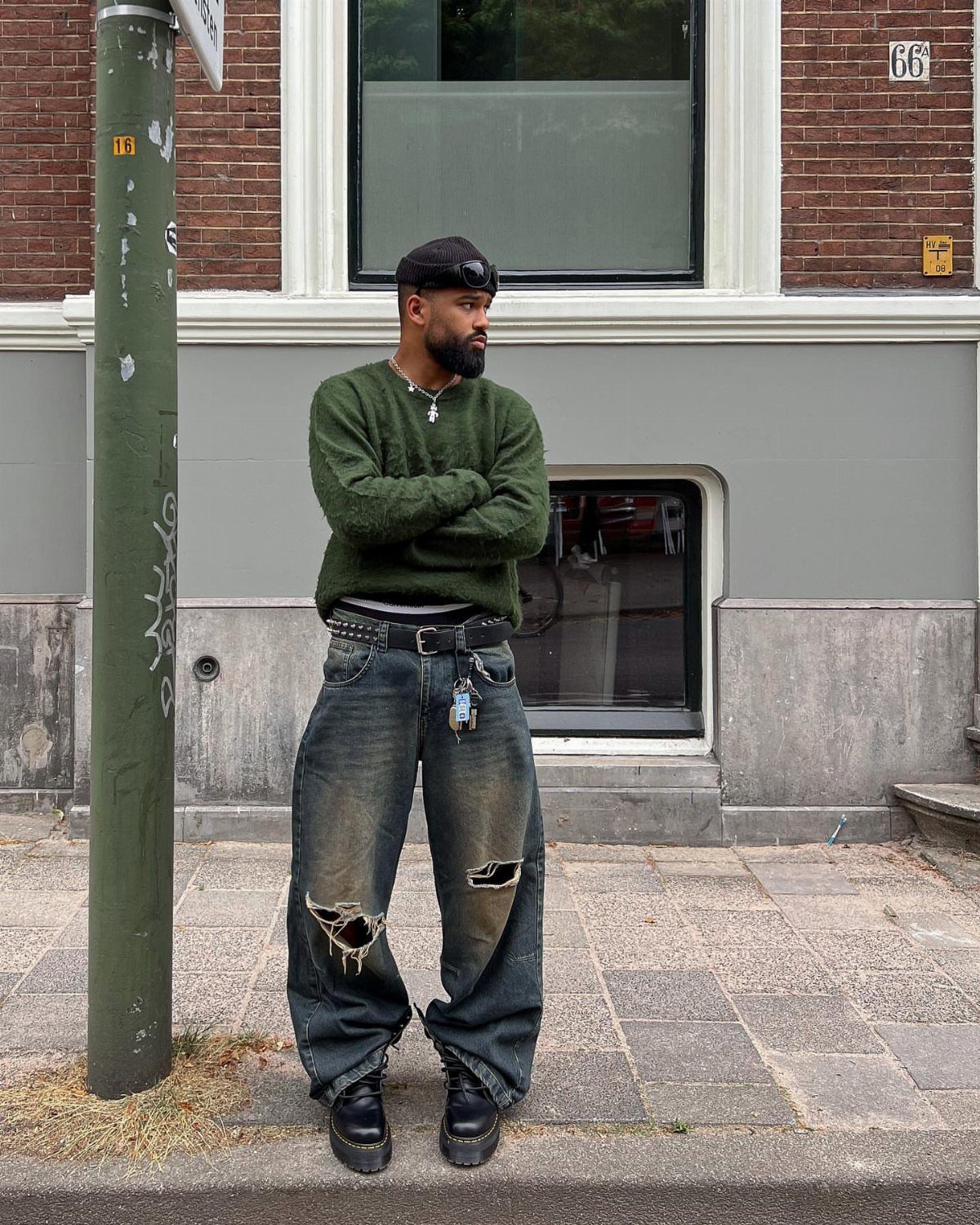 Man in green sweater and wide-leg distressed grey jeans standing on a sidewalk