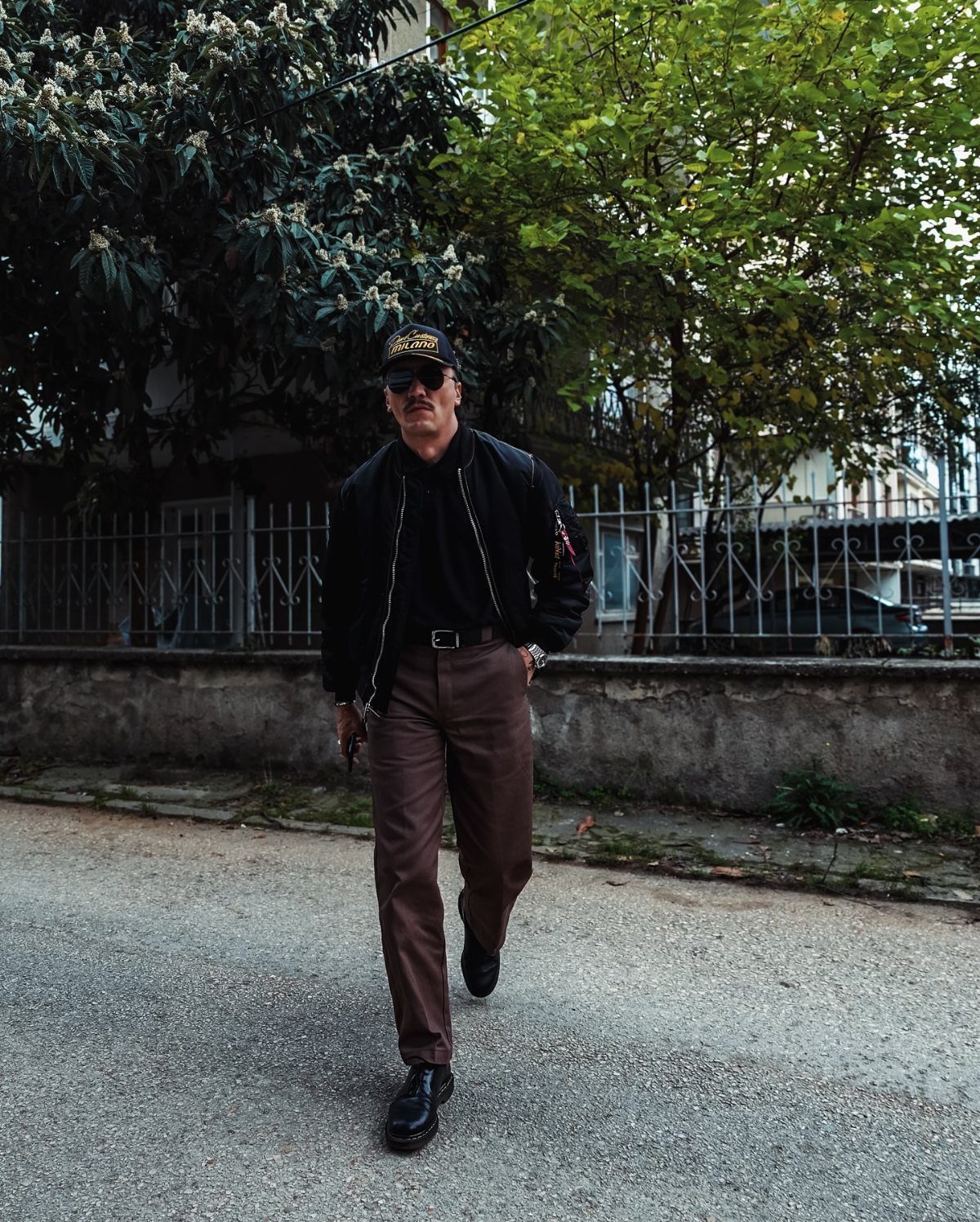 Man in black bomber jacket and brown trousers wearing black Dr Martens boots.