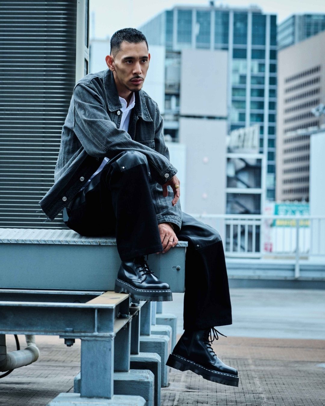 Man wearing chunky black platform boots and black denim pants sitting outdoors.