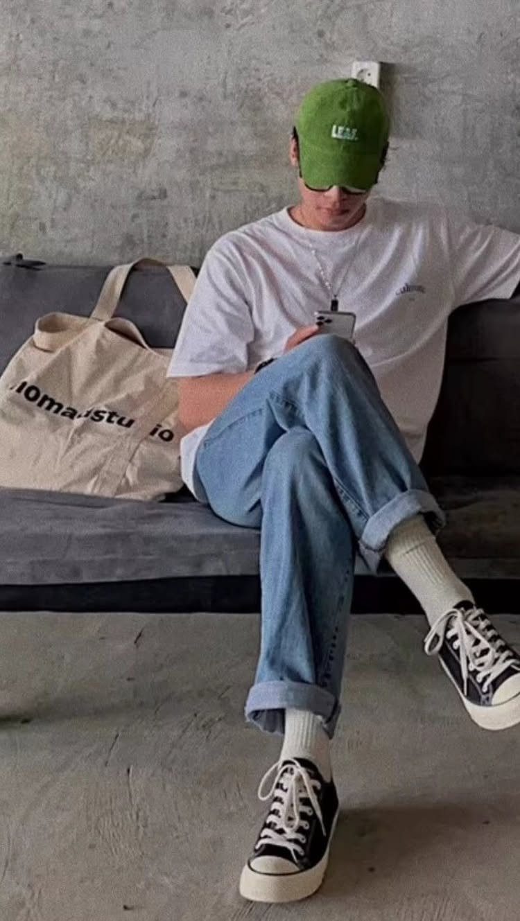 Man wearing black canvas sneakers, blue jeans, and a white t-shirt sitting on sofa