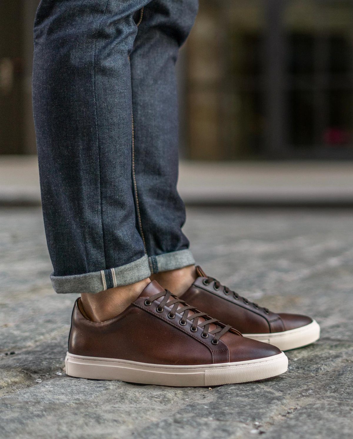 Brown leather low-top sneakers with white soles and cuffed blue denim jeans.