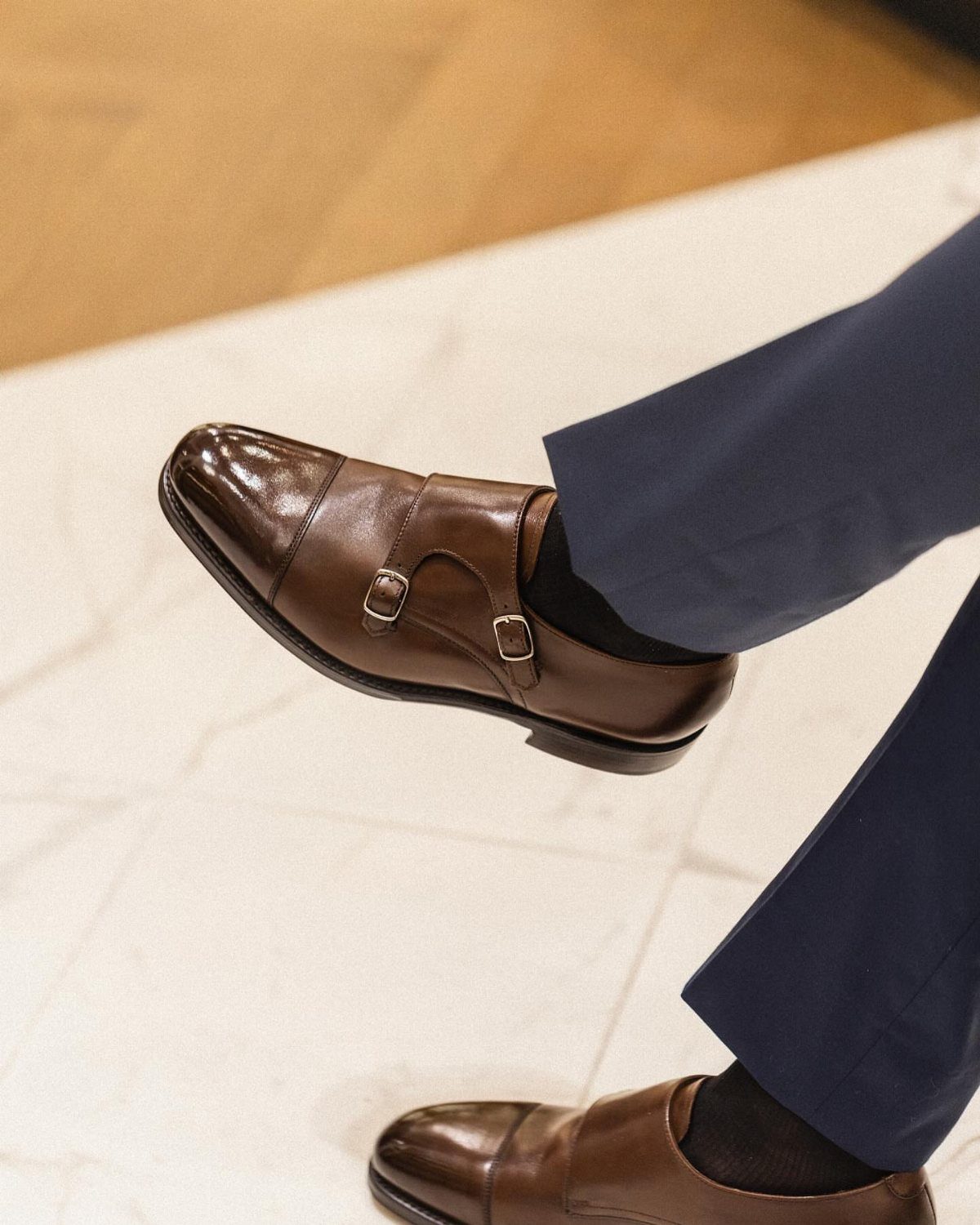 Brown leather monk strap shoes with buckles worn with navy blue trousers.