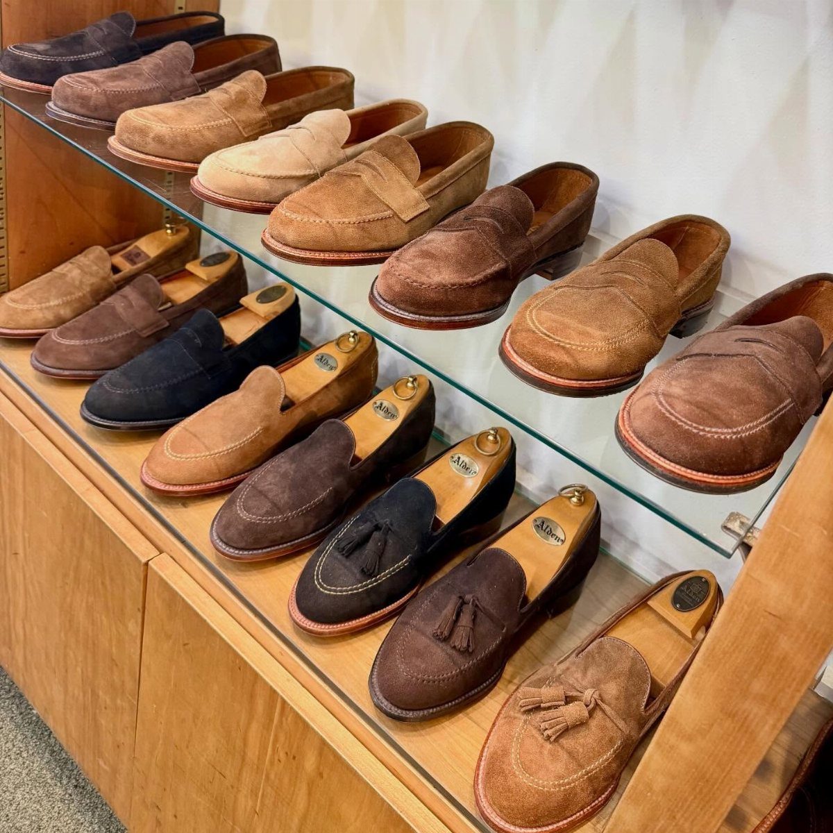 Suede loafers in various brown and black shades displayed on wooden shelves.