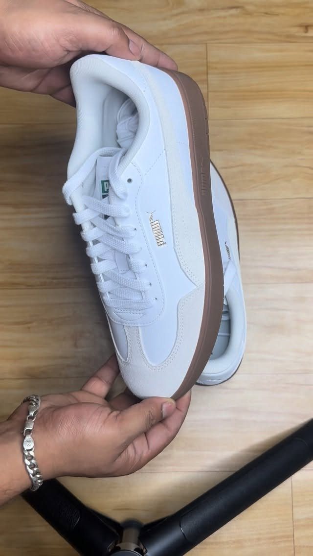 White Puma sneakers with brown soles held by hands over wooden flooring