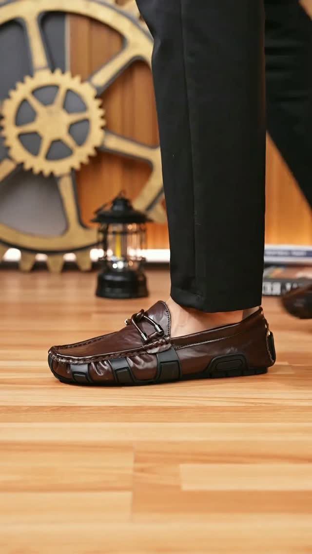 Brown leather driving loafers worn with black trousers on a wooden floor.