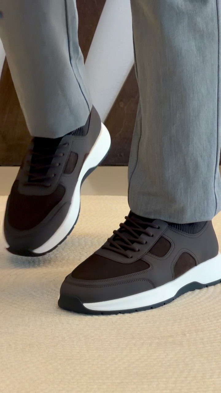 Dark brown hybrid dress sneakers with white soles and grey trousers.