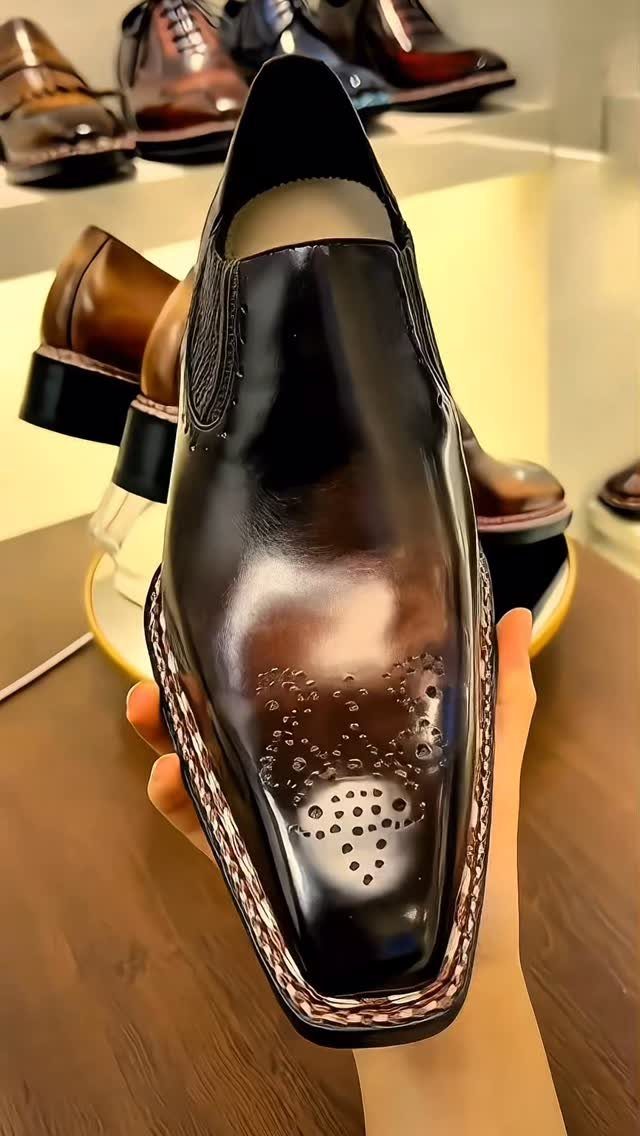 Polished dark brown leather slip-on dress shoe with decorative perforations on the toe.