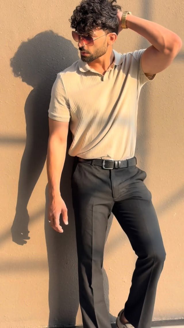 Man in beige polo and black trousers wearing a gold watch and sunglasses